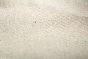Gros plan d'un tissu uni beige avec des fibres visibles et de petites taches sombres dispersées sur la surface.