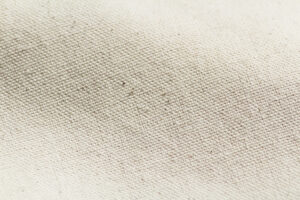 Vue rapprochée d'un tissu texturé blanc cassé avec des fibres tissées visibles et de petites taches.
