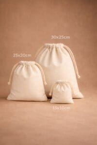 Trois sacs à cordon beiges de petite (15x10cm), moyenne (25x20cm) et grande (30x25cm) tailles sont présentés à la verticale sur un fond marron assorti.