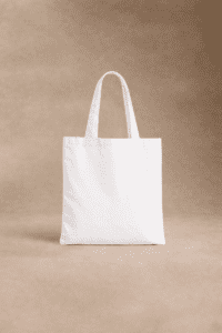 Un sac fourre-tout en toile blanche avec deux poignées se tient debout sur un fond beige neutre.