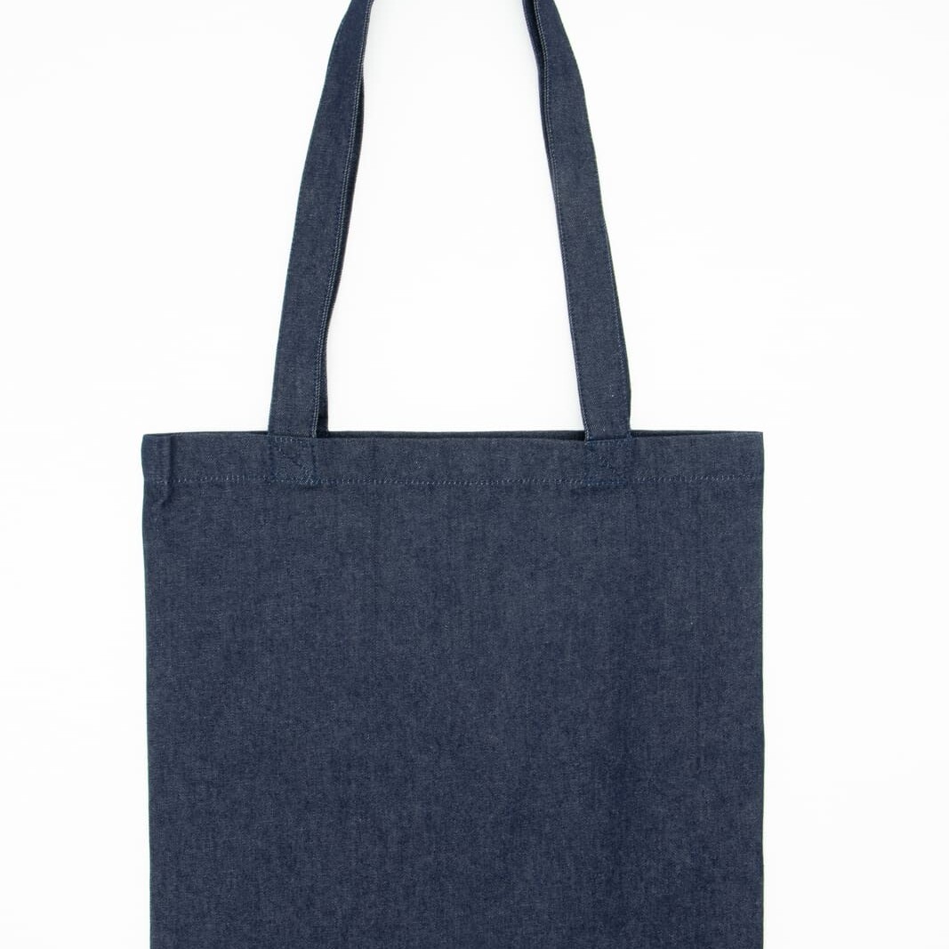 Ce sac fourre-tout en denim est doté de deux anses et arbore sur le devant une inscription blanche indiquant « SAC ÉTHIQUE Accessoire textile personnalisable ». Confectionné dans un élégant tissu denim noir, ce sac fourre-tout allie praticité et chic, ce qui en fait l'accessoire idéal pour un usage quotidien.