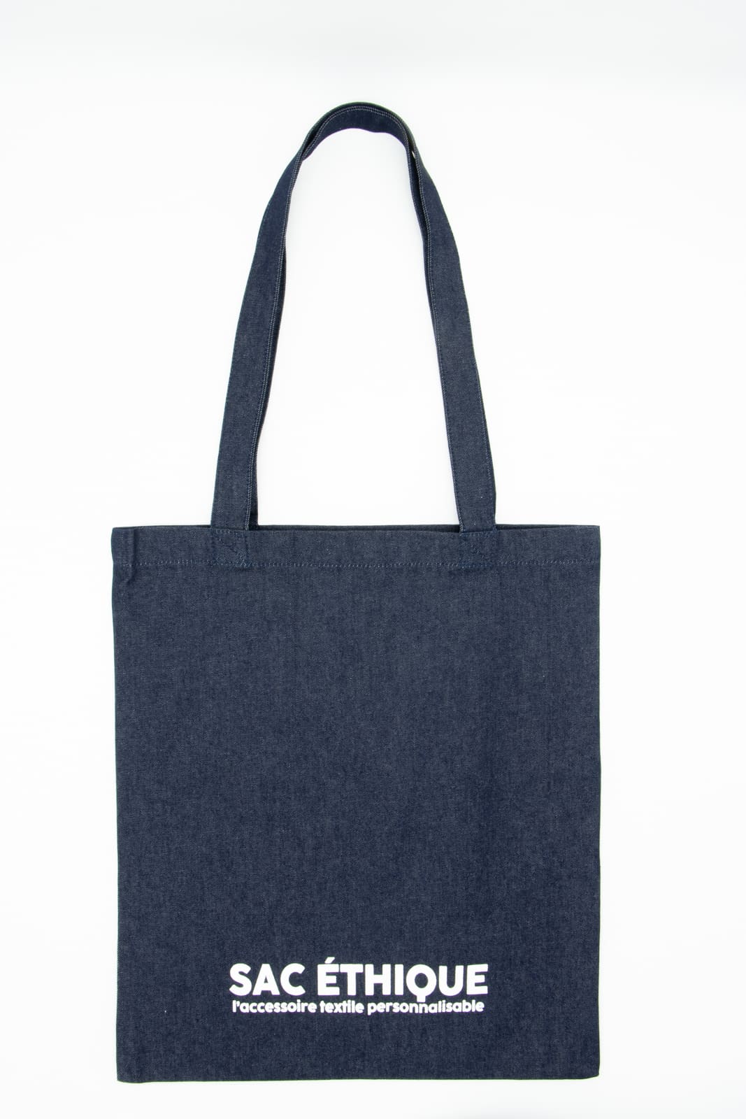 Ce sac fourre-tout en denim est doté de deux anses et arbore sur le devant une inscription blanche indiquant « SAC ÉTHIQUE Accessoire textile personnalisable ». Confectionné dans un élégant tissu denim noir, ce sac fourre-tout allie praticité et chic, ce qui en fait l'accessoire idéal pour un usage quotidien.