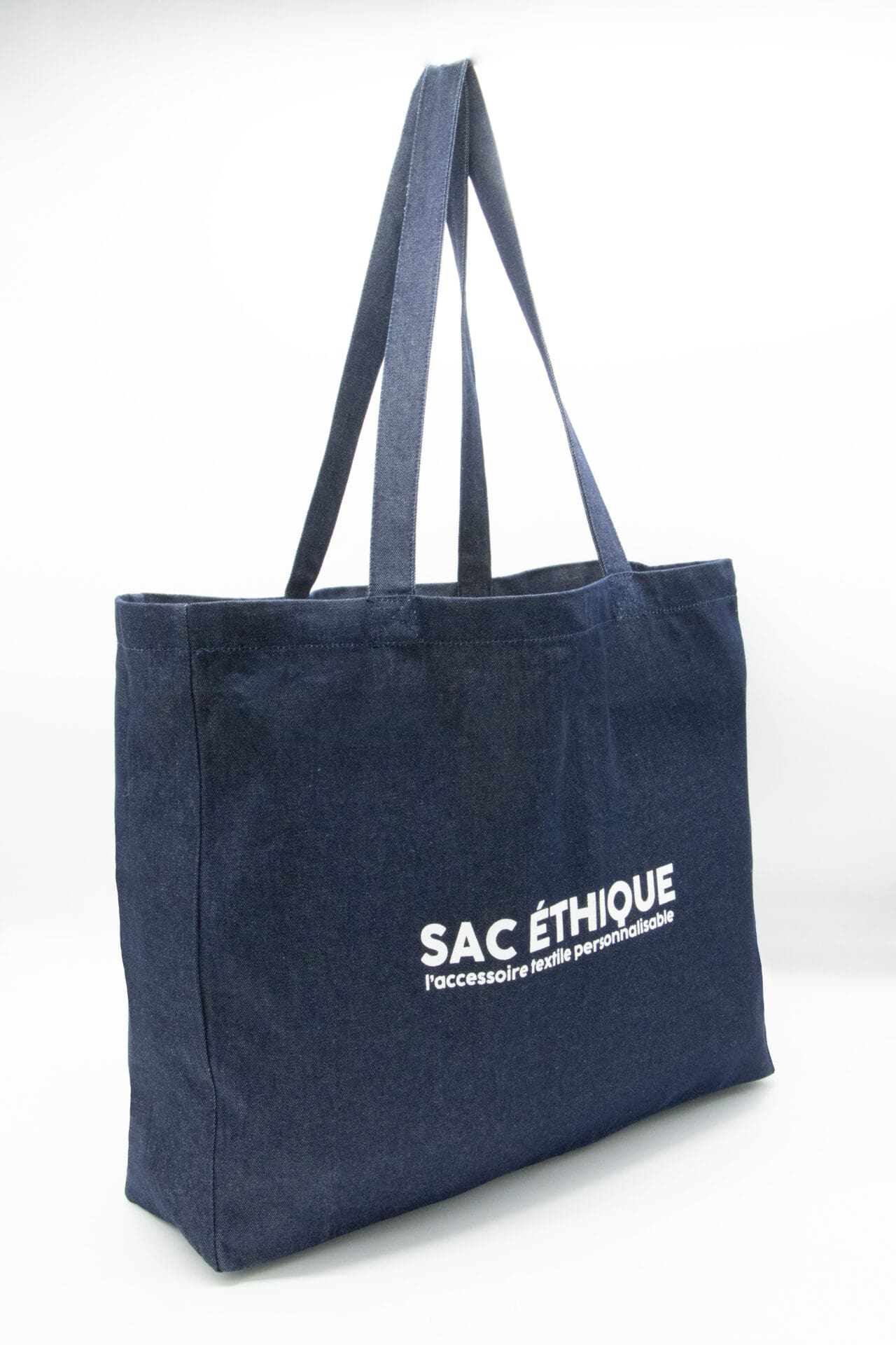 Un grand sac fourre-tout Cabas en denim bleu foncé, avec l'inscription « SAC ÉTHIQUE l’accessoire textile personnalisable » imprimée en blanc sur le côté.